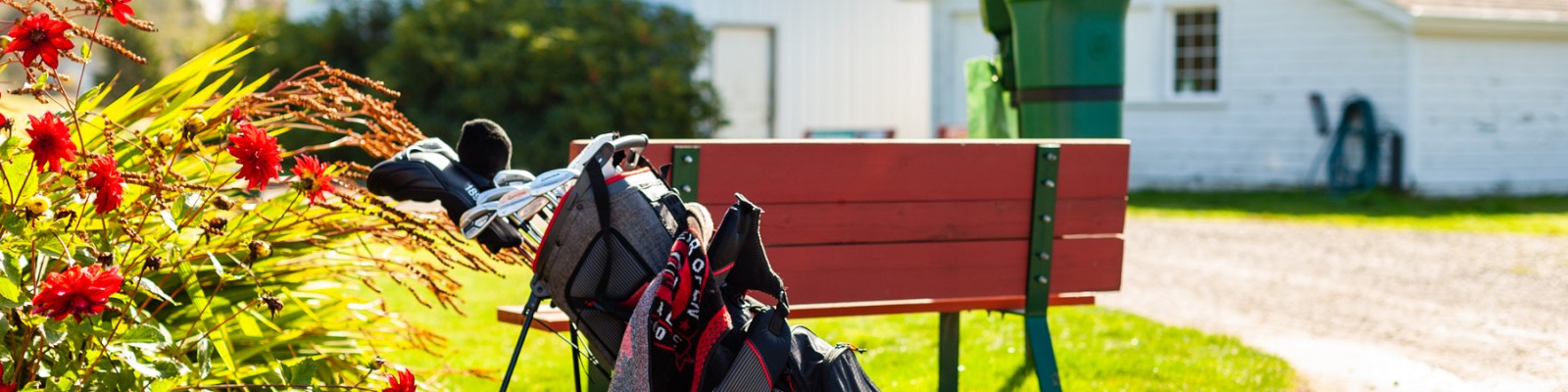 A golf bag rests beside a red bench near blooming flowers at Peninsula Golf Course, capturing a peaceful start to the round