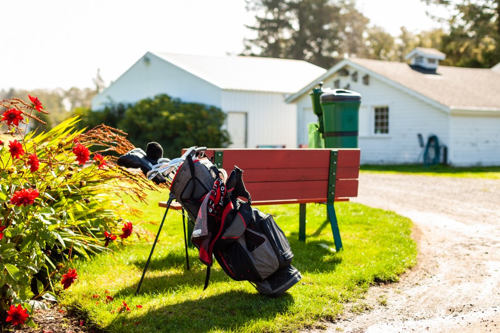 A golf bag rests beside a red bench near blooming flowers at Peninsula Golf Course, capturing a peaceful start to the round